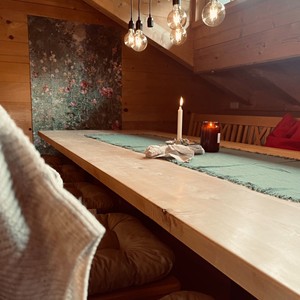 Langer Holztisch mit zwei brennenden Kerzen darauf.