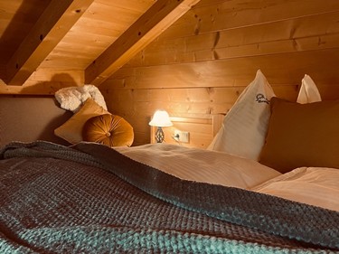 Bett im holzverkleideten Raum, beleuchtet von einer Nachttisch-Lampe.